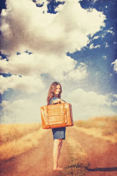 Брюнетка девушка с чемоданом на сельской дороге — стоковое фото