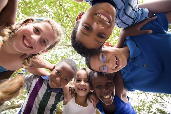 Дети обнимая в круге вокруг камеры и улыбается — стоковое фото