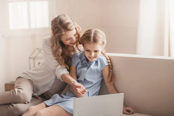 Счастливый мать и дочь, сидя на диване и используя ноутбук дома — стоковое фото
