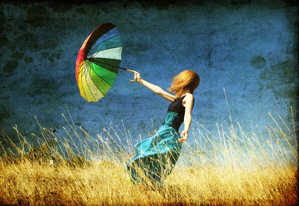 Рыжая девушка с зонтом на поляне ветреный трава — стоковое фото