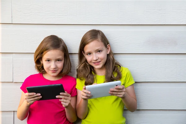 Сестра-близнец девочек играть с планшетный ПК счастливой на белой стене — стоковое фото