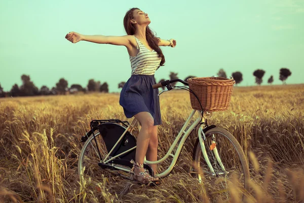 Свободная женщина пользуется свободой на велосипеде на пшеничном поле на закате — стоковое фото