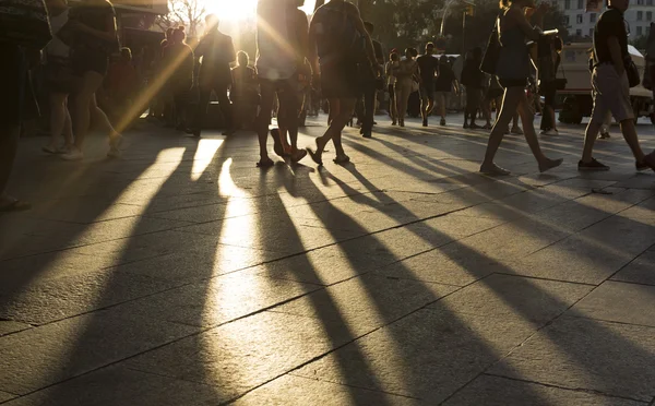 Толпы, ходить в районе города как солнечных вспышек между ними в конце второй половине дня создания длинные тени на земле — стоковое фото