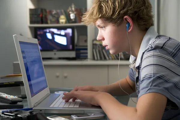 Молодой мальчик в спальне с помощью ноутбука и слушать MP3-плеер — стоковое фото