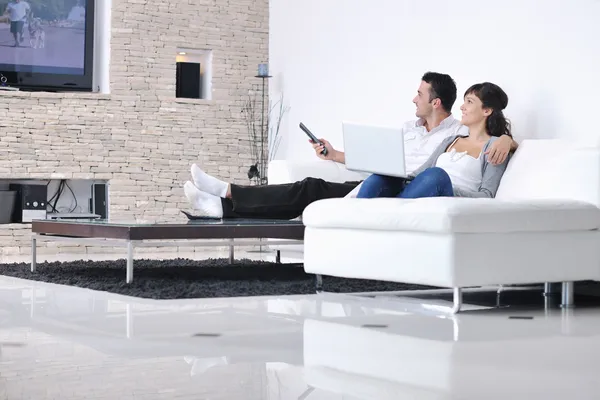Радостная пара расслабляется и работает над ноутбуком в современном доме — стоковое фото