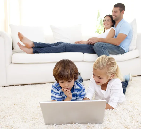 Дети, использующие ноутбук и родителей, лежащих на диване — стоковое фото